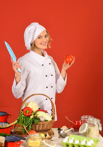 Professional cook in white suit standing at table holding knife and tomato in hands diet healthy