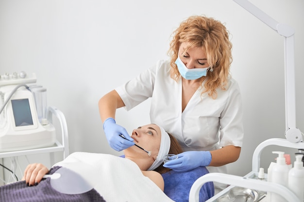 Professional cosmetologist is doing procedures for client in cabinet