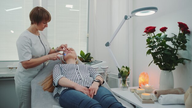 Professional cosmetologist making cavitation peeling on young woman's face