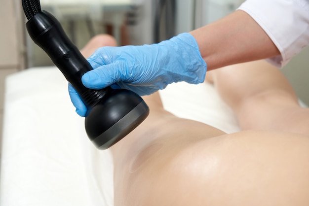 Professional cosmetologist using ultrasound cavitation machine on a female buttock