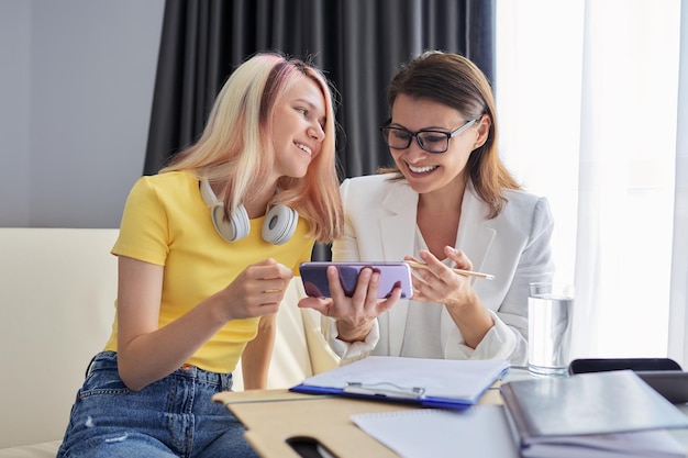 Professional counselor looks at smartphone screen with student girl