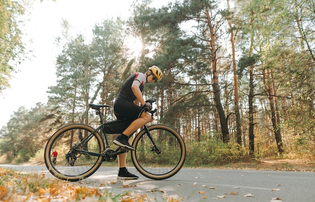 Professional cyclist in sport outfit stands with bicycle on country forest road on background