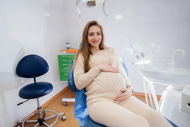 Dentista professionista tratta ed esamina la cavità orale di una ragazza incinta in un moderno studio dentistico. odontoiatria