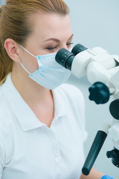 Professional dentist wearing a medical mask at her workplace and using a modern microscope