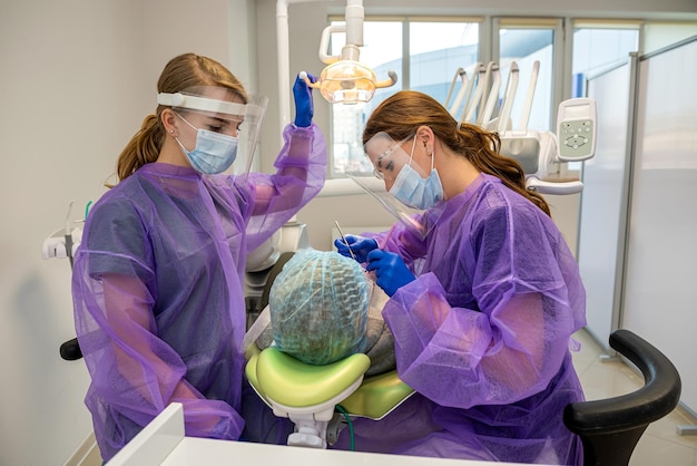 Professional dentist with assistant treats teeth young woman patient lying in a dental chair at a dental clinic