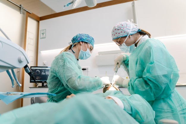 Professional dentists in latex gloves using clean tools to perform oral procedure on unrecognizable patient in contemporary clinic