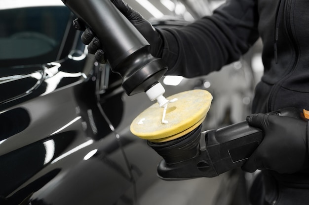 Photo professional detailing of the car in the auto studio the master applies paste or wax