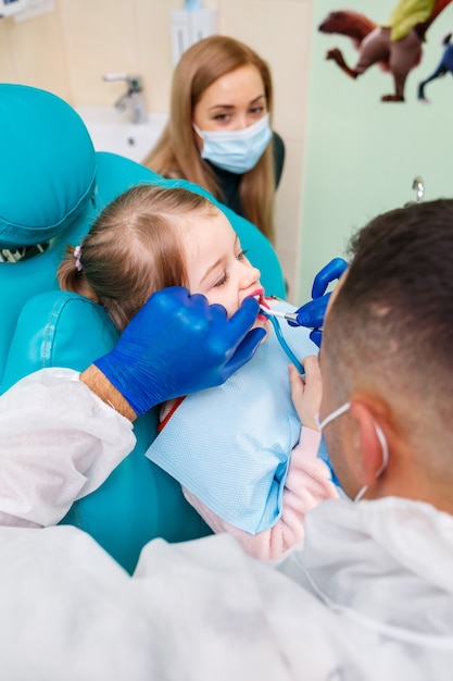 A professional doctor, a children's dentist, treats a little girl's teeth with instruments. Dental office for patient examination. The process of dental treatment in a child