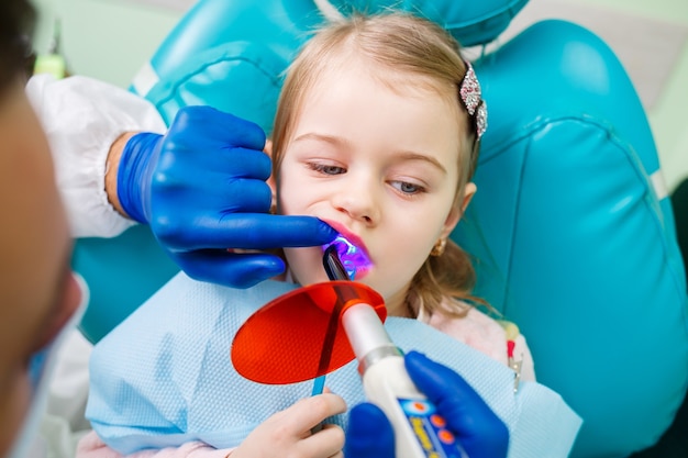 A professional doctor, a children's dentist, treats a little girl's teeth with instruments. Dental office for patient examination. The process of dental treatment in a child