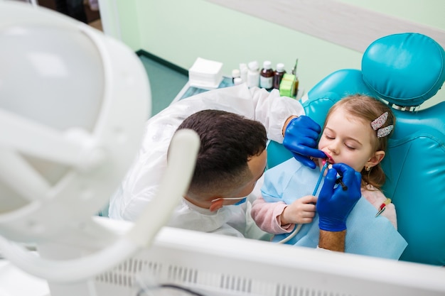 A professional doctor, a children's dentist, treats a little girl's teeth with instruments. Dental office for patient examination. The process of dental treatment in a child