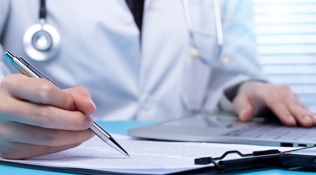 전문 의사는 병원 사무실에서 환자 약에 대한 의료 의료 문서에 서명합니다. 의사는 실험실 코트 유니폼을 입고 보험 사람과 메모 펜 복사 공간을 위해 책상에 있는 환자 차트를 읽습니다.