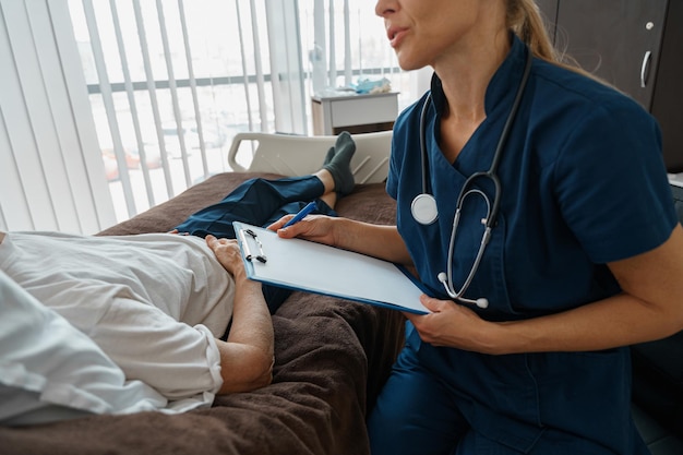 Professional doctor in uniform examines the patient during a\
visit to hospital ward