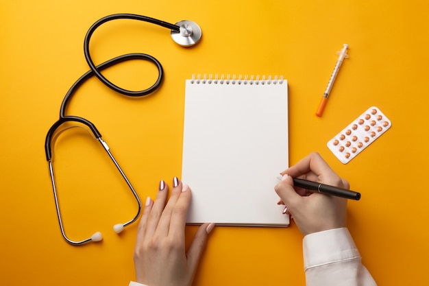 Medico professionista che scrive cartelle cliniche in un taccuino con stetoscopio, siringa e pillole. vista dall'alto con posto per il testo.