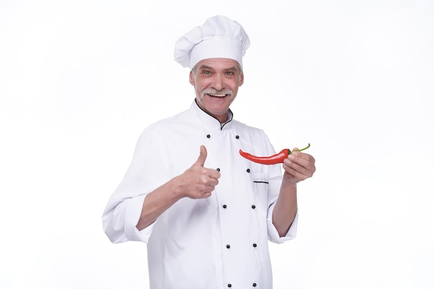 Professional elderly male chef with red pepper on white wall. Happy chef with vegetables