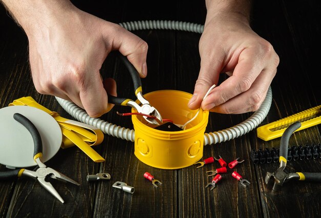 マスター電気技師のワークショップでの専門的な電気接続作業中の電気技師の手のクローズアップ黄色の接続箱で斜めペンチでケーブルまたはワイヤーを切断する