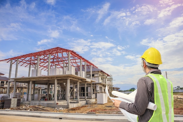 Professional engineer architect worker with protective helmet and blueprints paper at house building construction site background