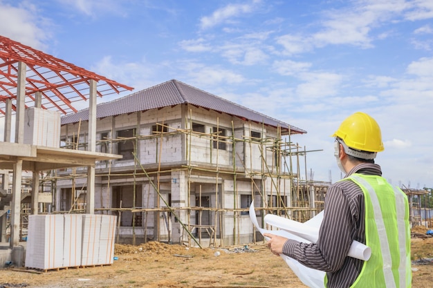 Professional engineer architect worker with protective helmet and blueprints paper at house building construction site background