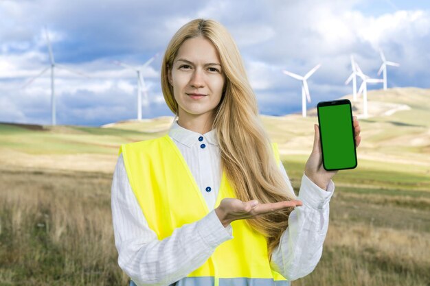 風力タービンの背景に緑色の画面を持つ携帯電話を持つプロのエンジニア