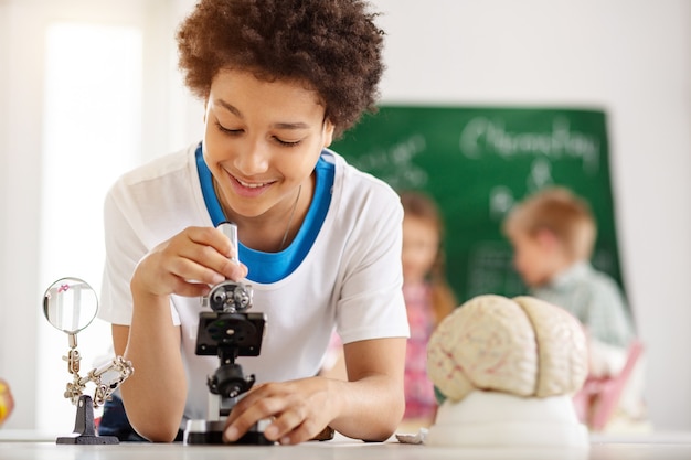 Professional equipment. Delighted nice boy using a microscope while being in the biological lab