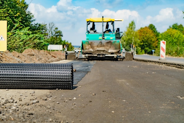 Professional equipment falls asleep by sand and rubble a reinforced mesh on the road Modern technology of construction and repair works of roads