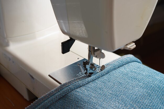 Professional equipment. Modern sewing machine with special pressure foot. The process of sewing a decorative edging cord of blue item of clothing.