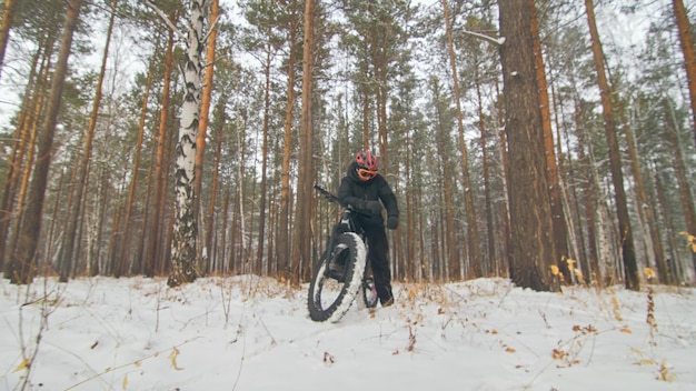 Il motociclista professionista di sport estremo si siede fatbike all'aperto il ciclista si sdraia nella foresta invernale