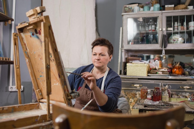 A professional female artist is engaged in painting on canvas in the studio The artist paints a picture in her studio