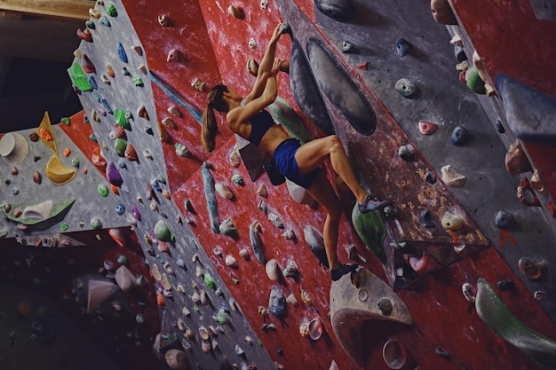 Professional female climber on a bouldering wall indoors.