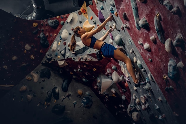 Photo professional female climber on a bouldering wall indoors.