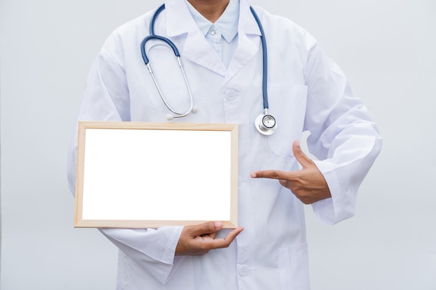 Professional female doctor in white coat over white isolated background and Pointing to white blank board.