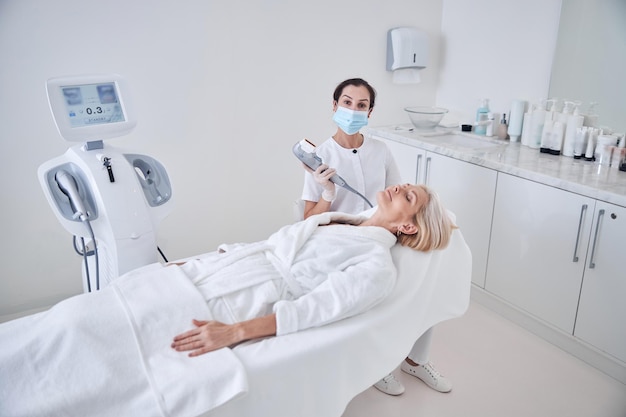 Professional female doctor working with patient while applying special ultrasound machine