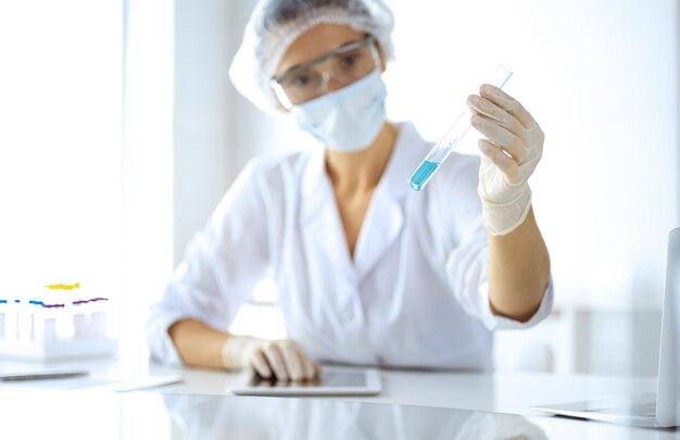 Professional female scientist in protective eyeglasses researching tube with reagents in laboratory. Concepts of medicine and research.