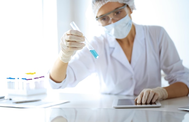 Professional female scientist in protective eyeglasses researching tube with reagents in laboratory. Concepts of medicine and research.