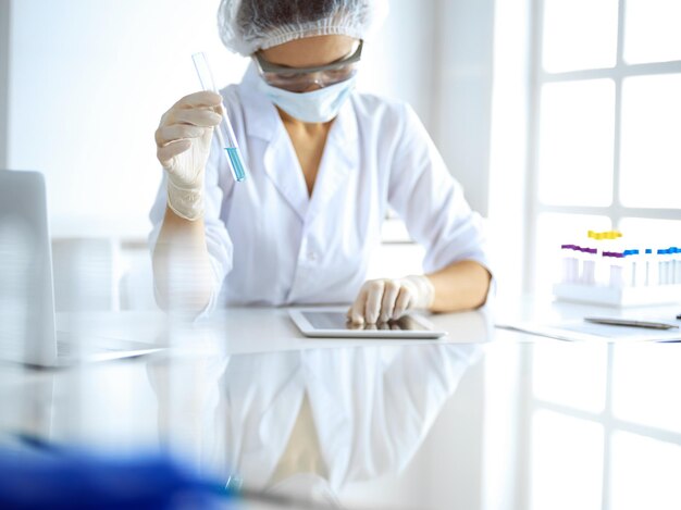 Professional female scientist in protective eyeglasses researching tube with reagents in laboratory. Concepts of medicine and research.