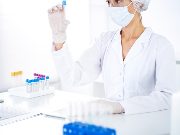 Professional female scientist in protective eyeglasses researching tube with reagents in laboratory. Concepts of medicine and science researching.