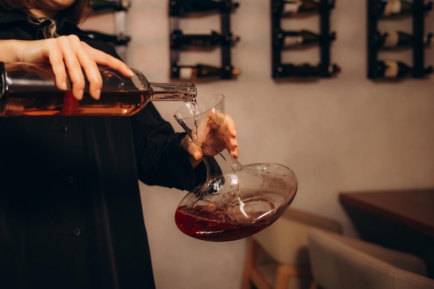 Профессиональная женщина-соммелье наливает красное вино из декантера в стакан.