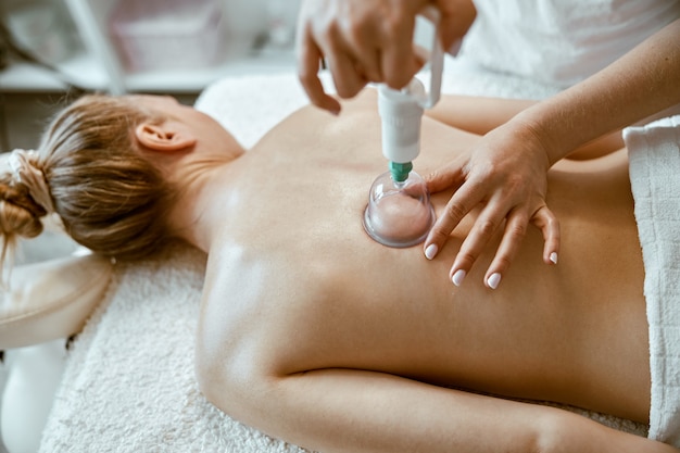 Professional female specialist is doing cupping therapy on the back of beautiful caucasian lady