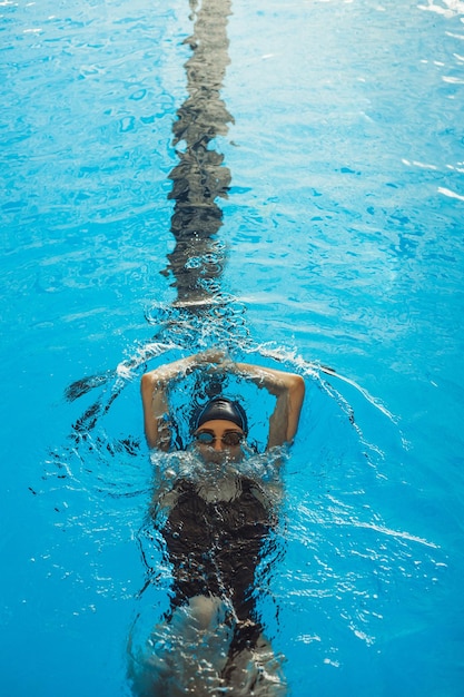 professional female swimmer in goggles and swimsuit showing Backstroke during swimming training