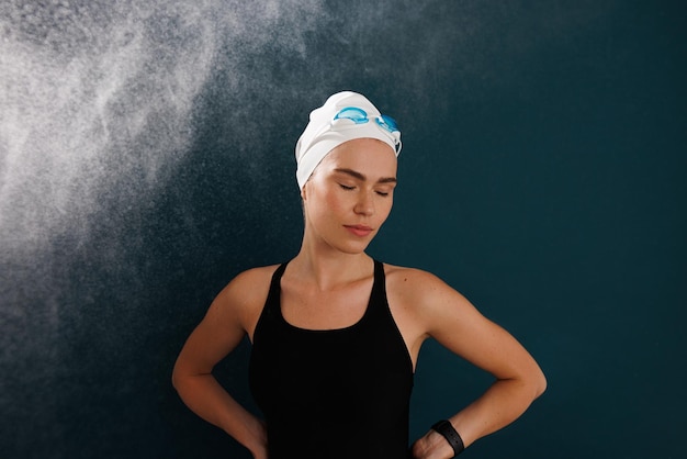 Professional female swimmer wearing a white swimming cap and goggles standing with closed eyes