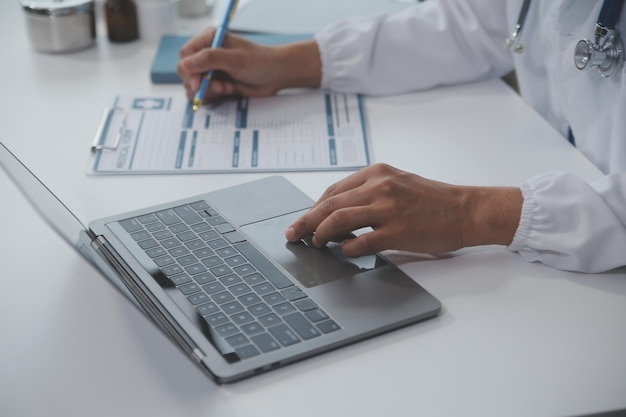 Foto una professionista e focalizzata medico donna asiatica in scrub sta lavorando e leggendo la ricerca medica sul suo laptop nel suo ufficio in un ospedale