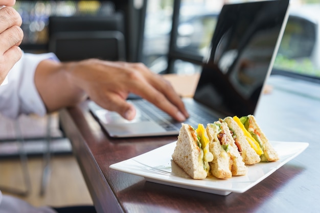 Professional gebruikt laptop naast clubsandwich in een café in Thailand.