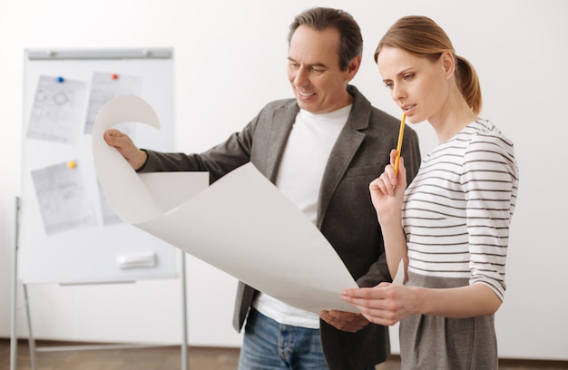 Professional glance. Pleasant skillful engineers holding a blueprint while working together on the project in the office