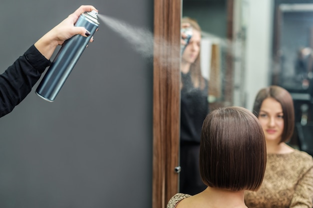 ビューティーサロンで短い髪型にヘアスプレーを適用するプロの美容師