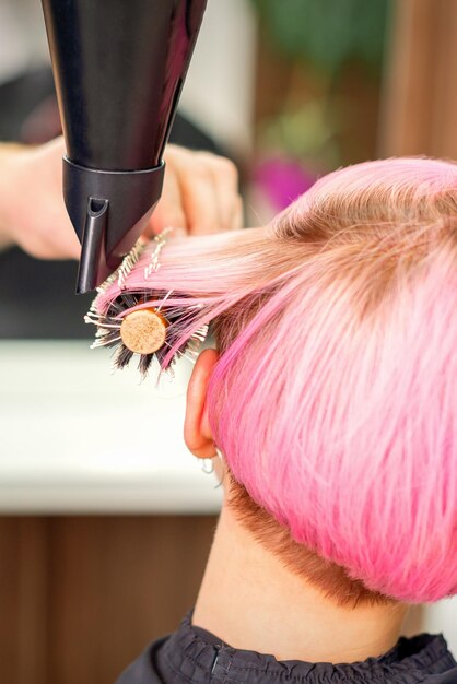 A professional hairdresser is drying long red hair with a hair dryer and round brush, close up.