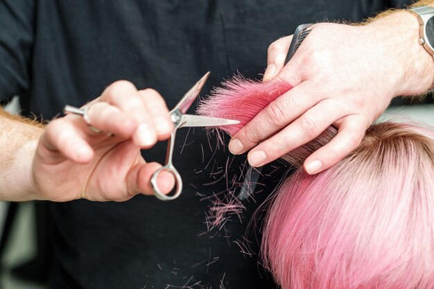 Professional hairdresser is holding in hand between fingers lock of red hair and cuts hair tips