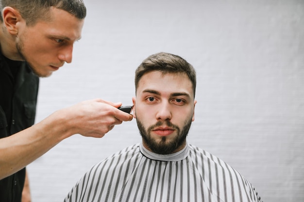 Профессиональный парикмахер делает стильную прическу для красивого клиента в мужской парикмахерской