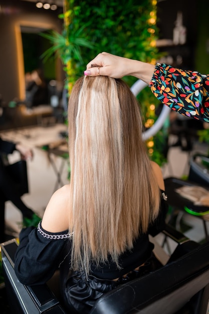 A professional hairdresser prepares blond hair for extensions in a beauty salon while trying it on for a client