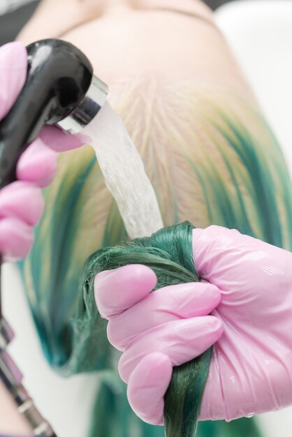 Professional hairdresser washes long green hair of client in sink with water from shower Working hai