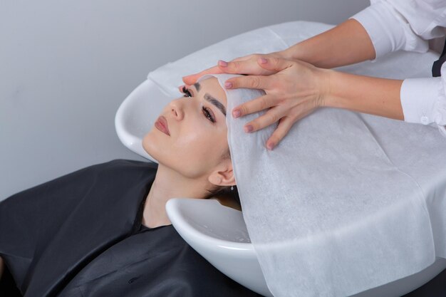 professional hairdresser washing hair of young woman in beauty salon