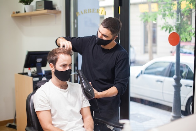 코로나 바이러스 동안 고객에게 머리카락을 자르는 보호 마스크를 착용 한 전문 미용사